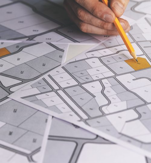 hand with pencil on cadastral map - choose and buy a building plot for house construction